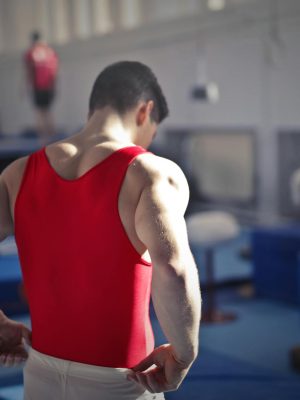 Back view of muscular athlete in red uniform preparing for training in gymnast hall with equipment